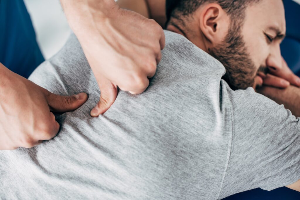 chiropractor massaging back of bearded man in hospital